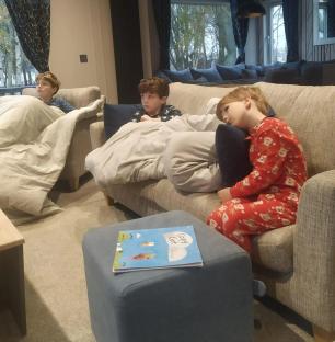 Three boys relaxing under blankets on a couch.