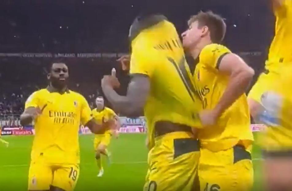 Soccer players celebrating a goal with one player biting the other's shirt.