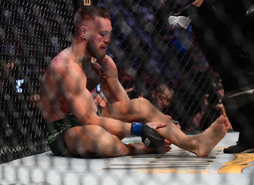 Conor McGregor holding his injured leg in the octagon.