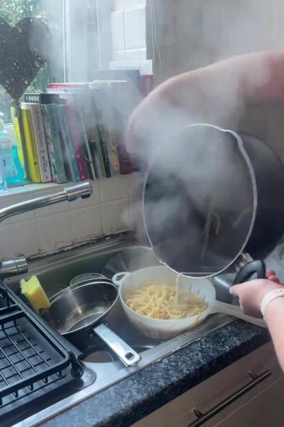 A person draining pasta in a kitchen sink.