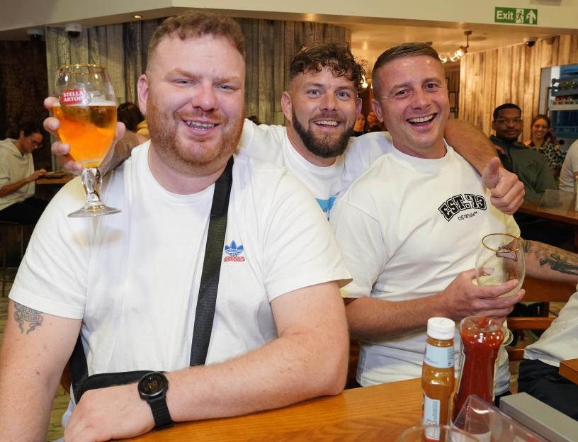 Three men at a pub, smiling and holding beers.