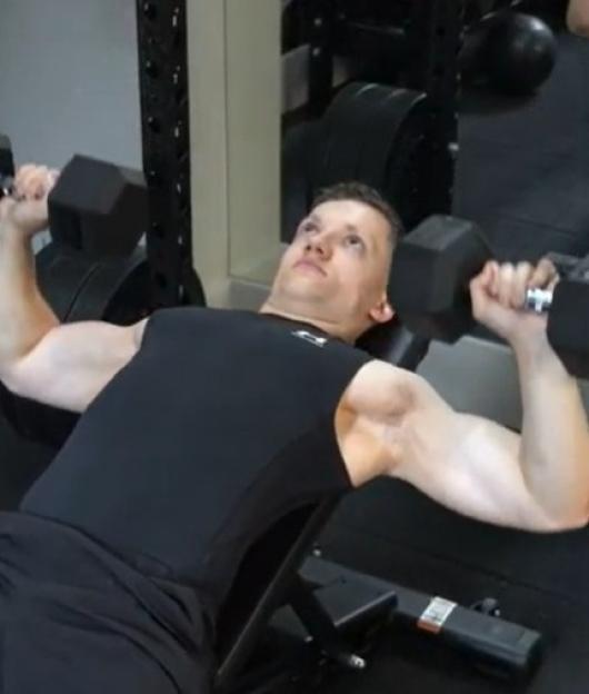 Man doing a dumbbell incline press in a gym.