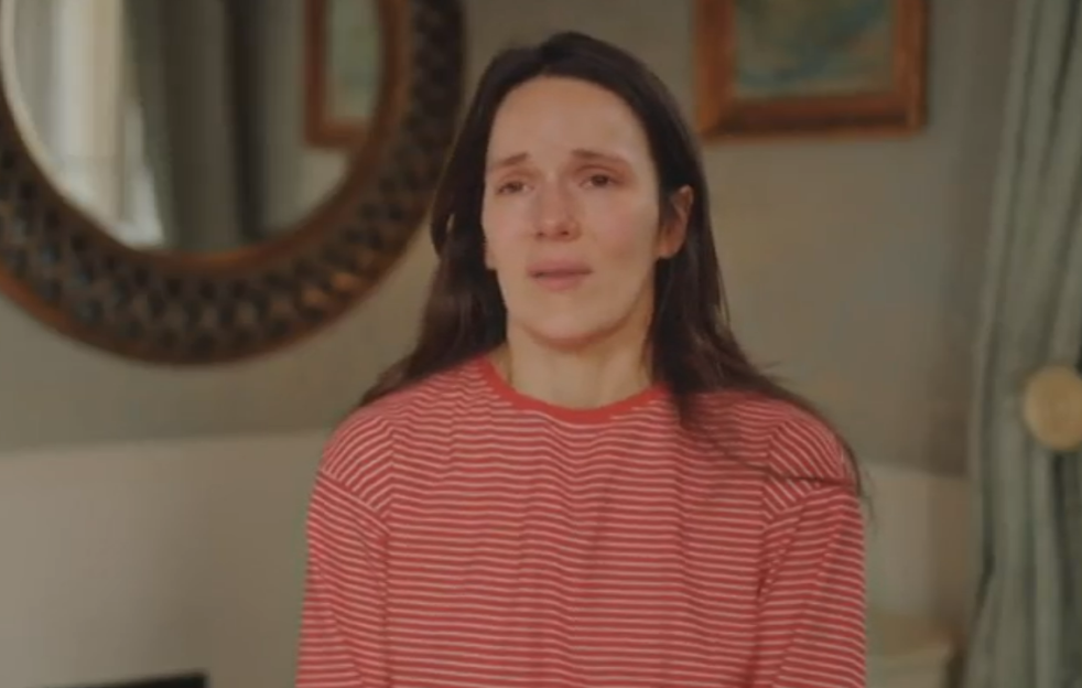 A woman with long dark hair, wearing a red and white striped shirt, appears to be crying.