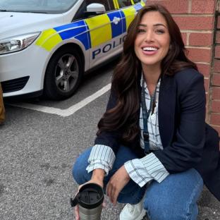 Woman crouching beside a police car, holding a travel mug.