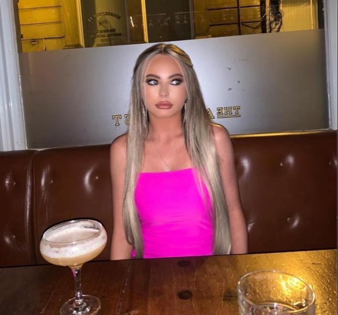 Woman in pink dress sitting at a table with a cocktail.