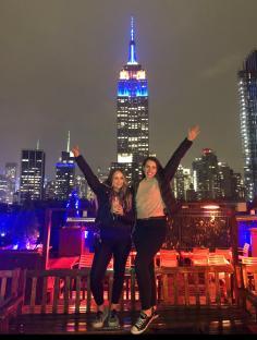 Two women on a rooftop bar in New York City with the Empire State Building in the background.