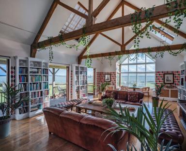 Interior of a large room with high ceilings, exposed wooden beams, leather sofas, and bookshelves.