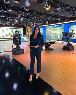A woman in a navy pantsuit stands in a television studio.