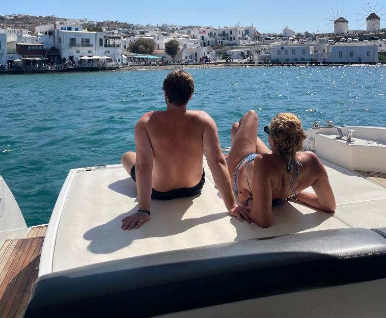 Lucy Holden and her boyfriend relaxing on a boat with a coastal town in the background.