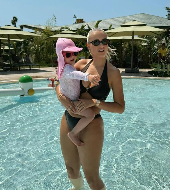 Molly-Mae Hague in a black bikini holding a baby in a pool.