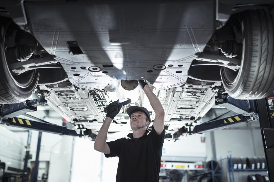 A mechanic examines the underside of a car on a lift.