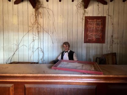 Mannequin behind a dusty counter in an abandoned Western-themed town.