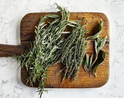 Rosemary, thyme, and sage sprigs on a wooden cutting board.