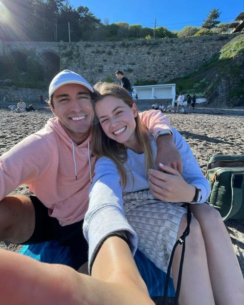 South African influencer Jeanni Mulder and rugby player Greg O'Shea pose for a selfie on a beach.