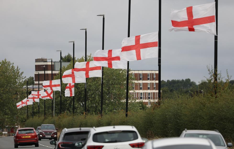 Several St. George's flags fly from lampposts along a road.