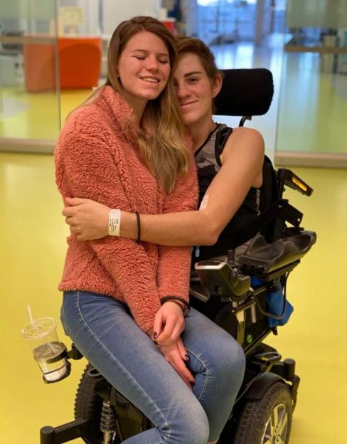 Sabia Reiche sitting on Loren Schauers' lap in his wheelchair, embracing each other and smiling.