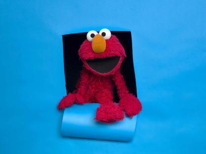 Elmo peeking through a hole in a blue background.