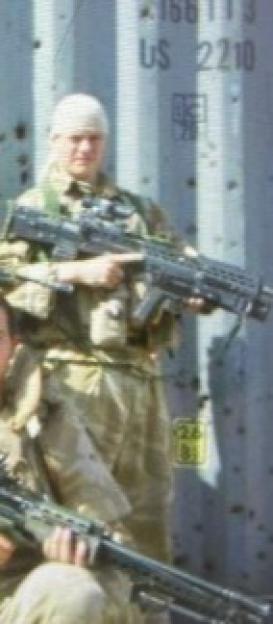 Two soldiers posing with large weapons in front of a bullet-ridden container.