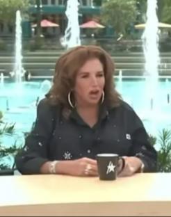Screenshot of a woman talking, with a fountain in the background.