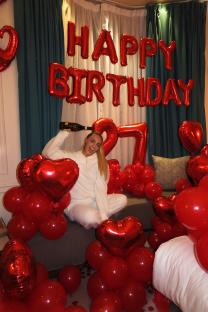 Woman celebrating her 27th birthday surrounded by red balloons.