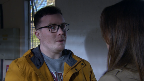 Screenshot of a man in glasses speaking to a woman.