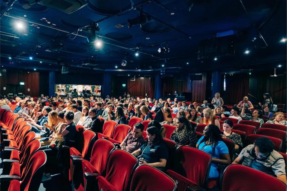 Audience in a dark theater with red seats.