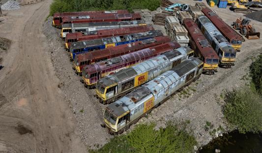 Aerial view of a dozen rusty diesel locomotives abandoned in a quarry.