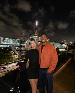 Couple posing on a rooftop overlooking a city skyline at night.