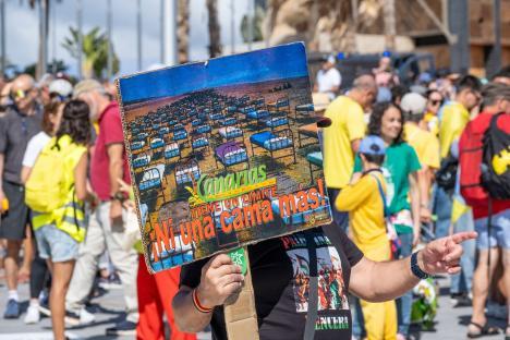 Protestor holding sign depicting hotel beds on a beach; text on sign reads