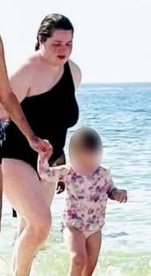 Woman on beach holding a child's hand.