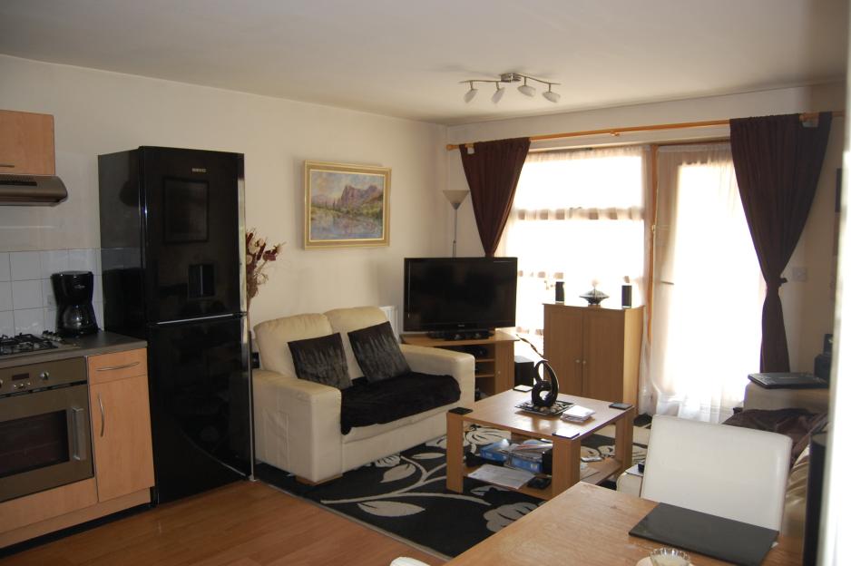 Stephen Port's flat in Barking, east London, showing a kitchen area with an oven and black refrigerator, and a living area with a cream-colored sofa, coffee table, and television.