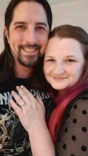 A woman showing off her engagement ring while embracing her fiancÃ©.