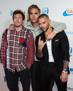 Three members of the band Busted posing for photos backstage.