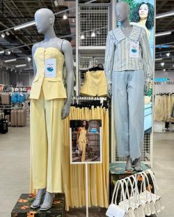 Mannequins displaying pastel yellow pantsuit and light blue striped shirt with jeans; prices shown.