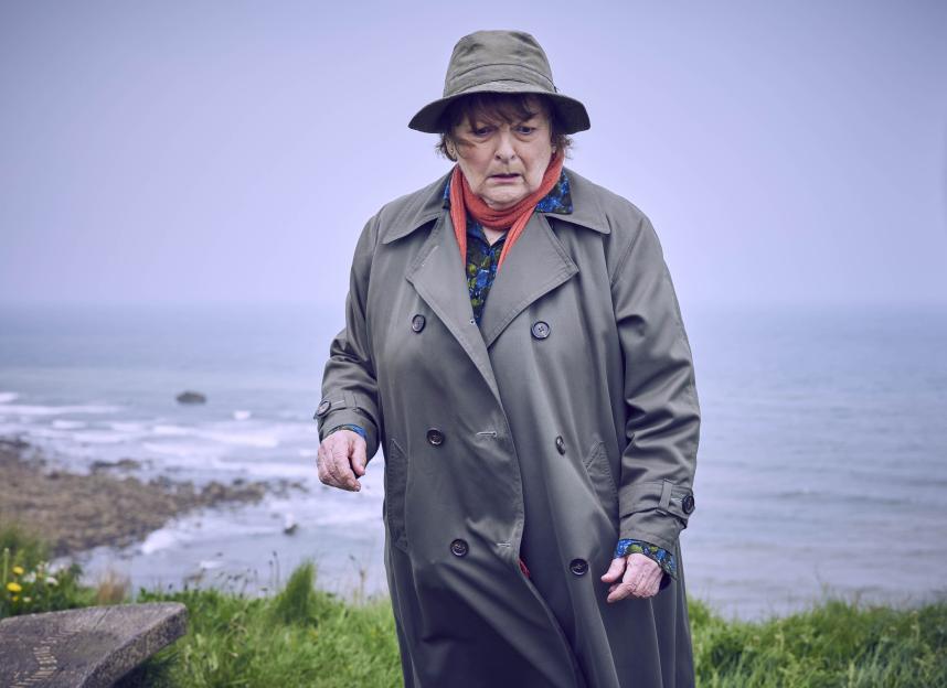 Brenda Blethyn as DCI Vera Stanhope in a trench coat and hat, standing by the sea.