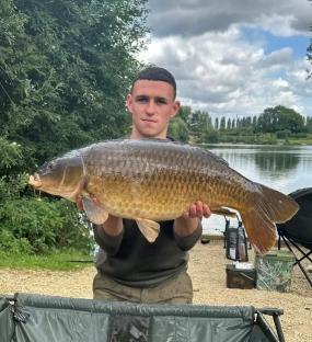 Man holding a large carp by a lake.