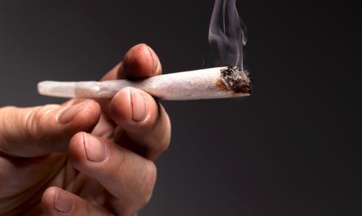 Close-up of a hand holding a lit marijuana joint.