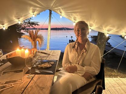 Woman sitting at a table outdoors at sunset, enjoying a meal.