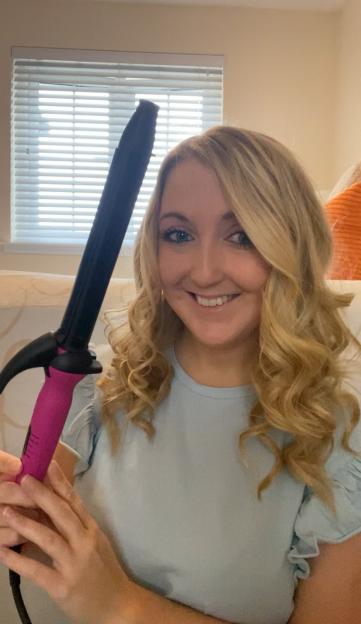 A smiling blonde woman holding a curling iron.