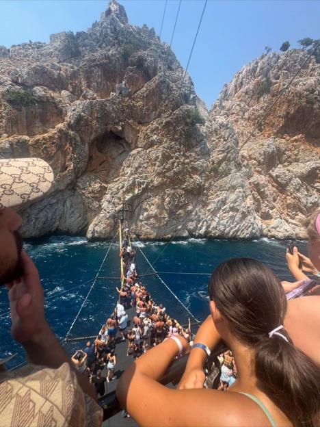 A boat full of people sailing past mountains on the water.