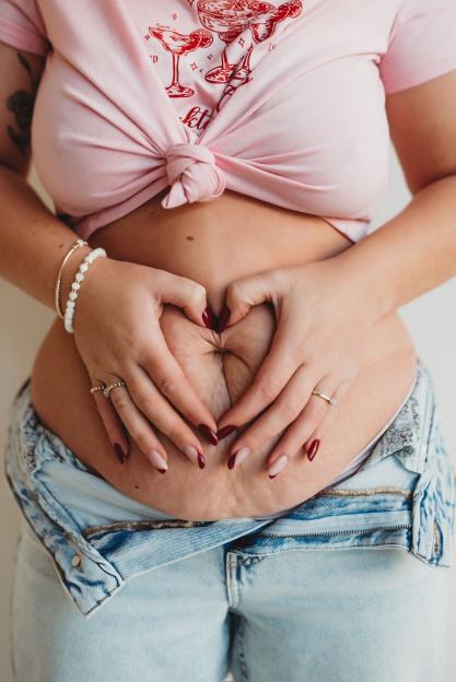Person's hands forming a heart shape on their abdomen.