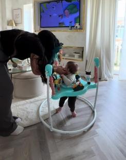 Woman interacting with baby in a baby walker in front of a TV.