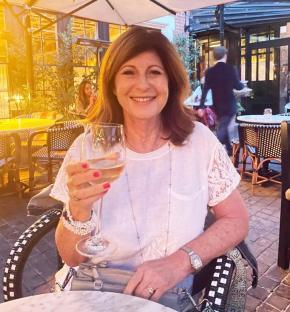 A woman sits outdoors at a cafe, holding a glass of white wine.