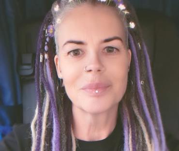 Close-up selfie of a woman with purple and gray dreadlocks.