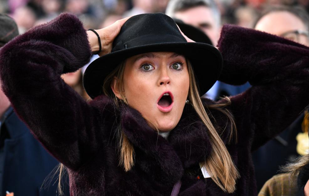 Racegoer Jodie O'Leary reacts with a shocked expression, holding her black hat, after watching a horse fall at the Cheltenham Racing Festival.