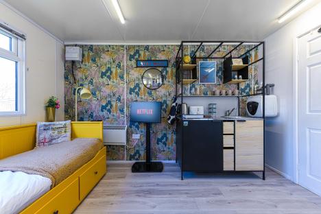 Interior of a small home built inside a converted airplane, featuring a yellow daybed, a kitchenette, and a Netflix-enabled TV.