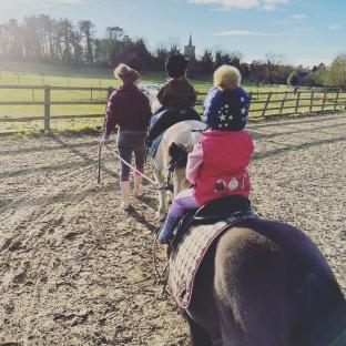 Children riding ponies, led by an adult.