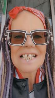 Close-up of a woman with missing teeth, wearing oversized sunglasses and a red bandana.