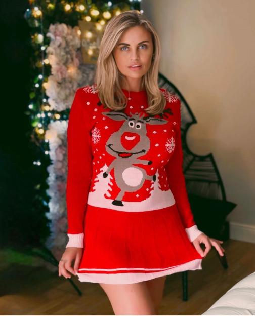 Carla Bellucci in a red Christmas sweater with a reindeer design, standing in front of a Christmas tree.