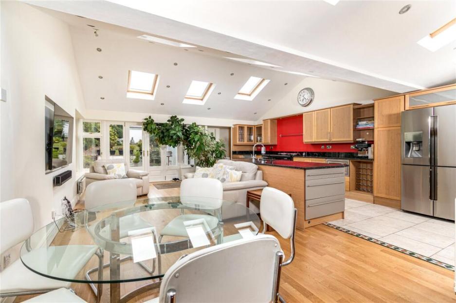 An open-plan kitchen and living room with wooden floors, a glass dining table, beige sofas, and a red kitchen wall.